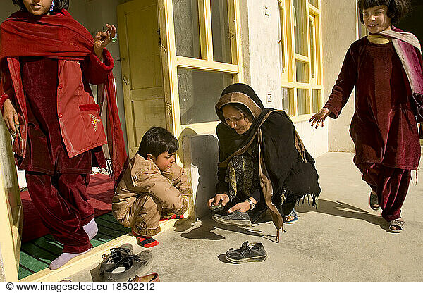 Woman helps her son clean his shoes in Kabul.