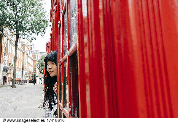 Woman hiding behind telephone booth in city