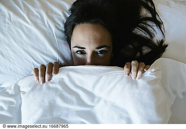 Woman hiding behind the sheet in bed