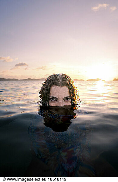 Woman hiding face in water at beach on sunset