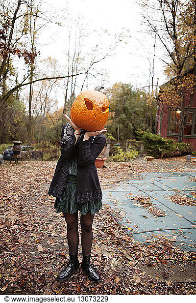 Woman hiding face with Halloween pumpkin while standing on field