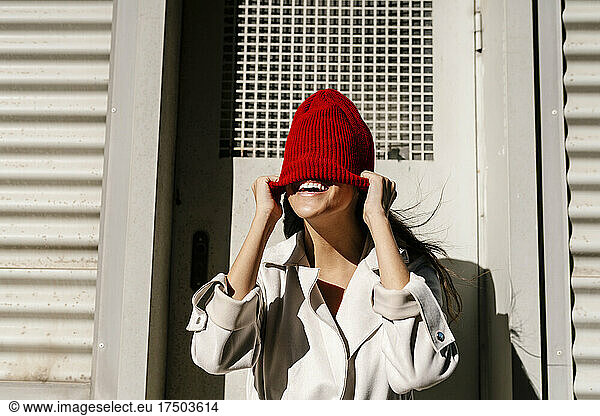 Woman hiding face with knit hat in front of door