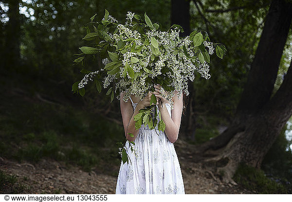 Woman hiding face with plants while standing in forest