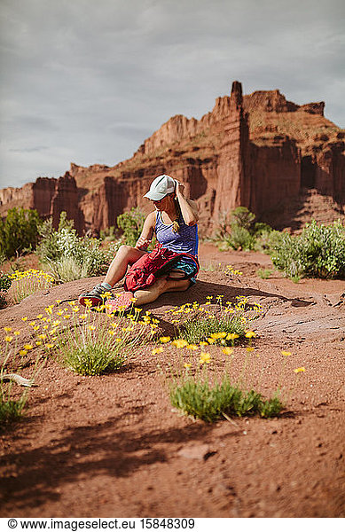 woman hiker adjust her hat while resting amongst yellow desert flowers
