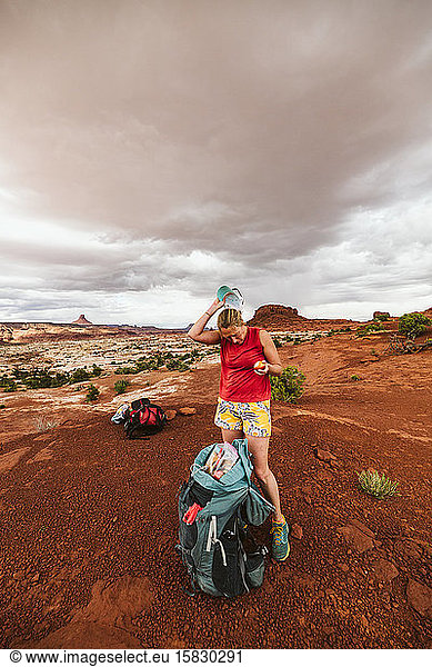 woman hiker eats apple and takes off her hat under stormy sky in utah