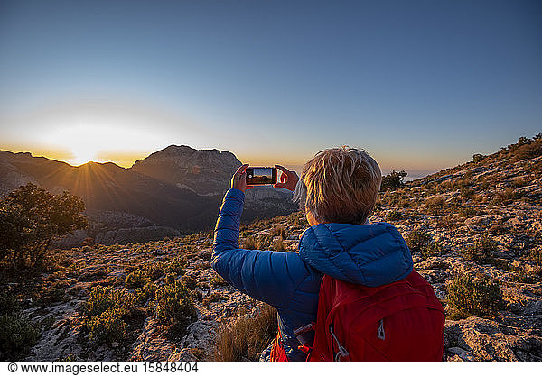 Woman hiking and taking a picture of the Puig Campana mountain.
