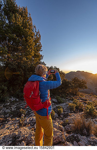 Woman hiking and taking a picture of the Puig Campana mountains.