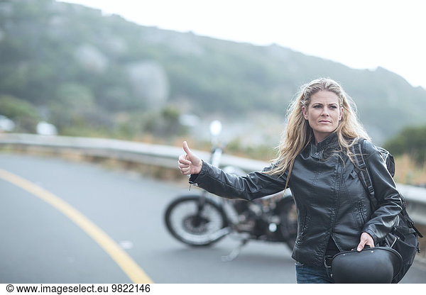Woman hitchhiking next to motorcycle on the road