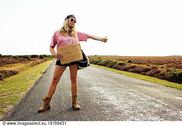 woman hitchhiking with a sign saying take me to happiness