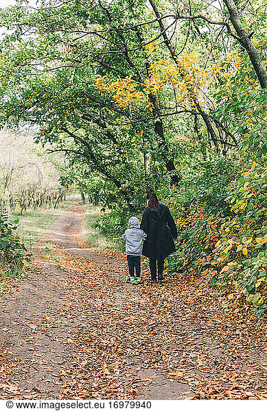 Woman hold little boy driving scooter at beautiful autumn path