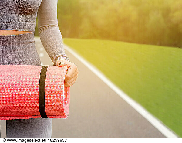 Woman hold pink mat for doing yoga on park in summer.