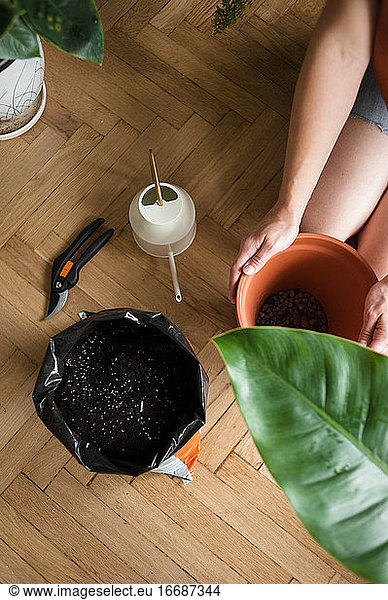 Woman hold pot with drainage next to soil and watering can on floor