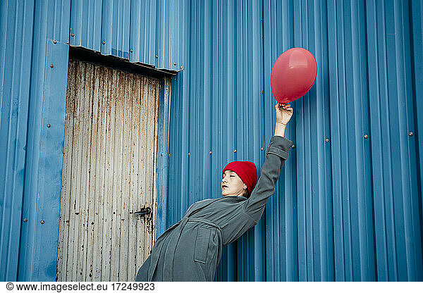 Woman holding balloon while bending over backwards on blue shutter