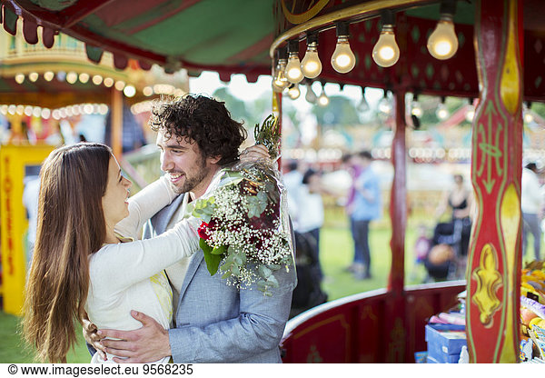 Woman holding bouquet and embracing his boyfriend in amusement park