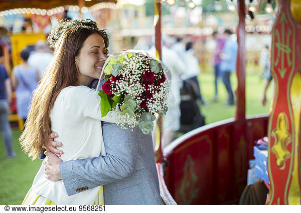 Woman holding bouquet and embracing his boyfriend in amusement park