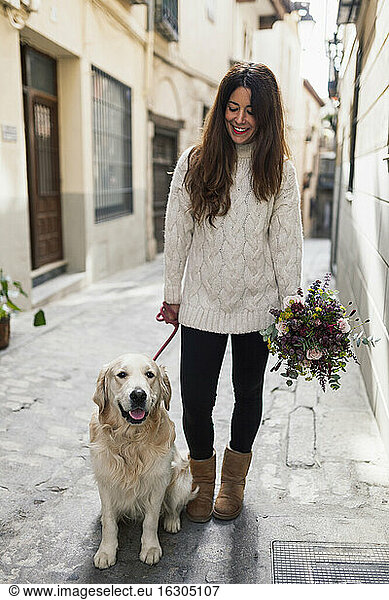 Woman holding bouquet while standing with dog on road in city