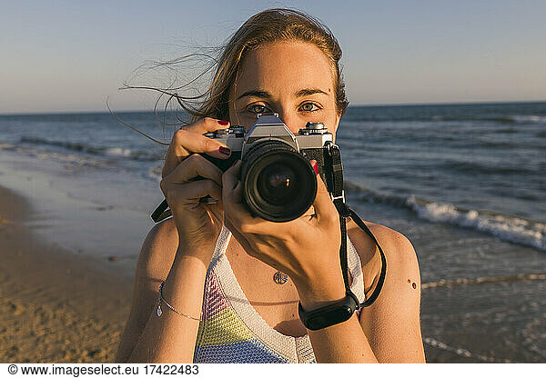 Woman holding camera near sea at beach