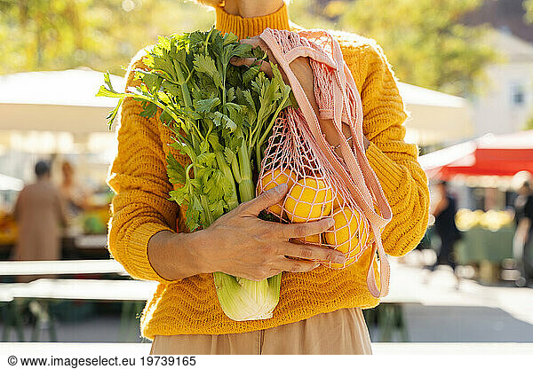 Woman holding celery and mesh bag with tangerines at farmer's market
