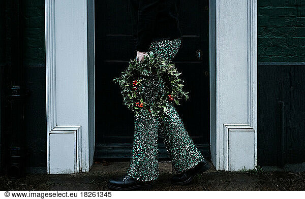 Woman holding Christmas wreath with sparkly trousers on
