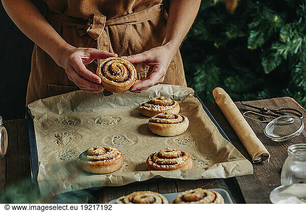 Woman holding cinnamon bun from tray at table
