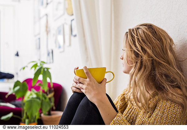 Woman holding coffee cup while sitting against wall