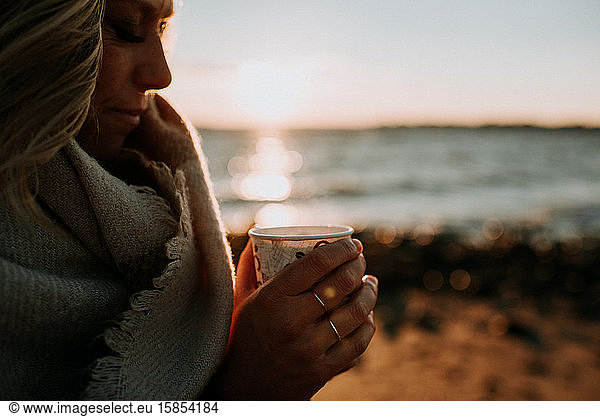 woman holding cup of coffee on beach at sunset