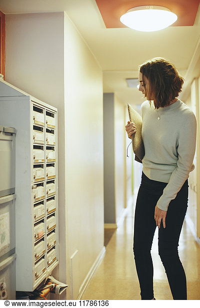 Woman holding document looking at mailbox in corridor