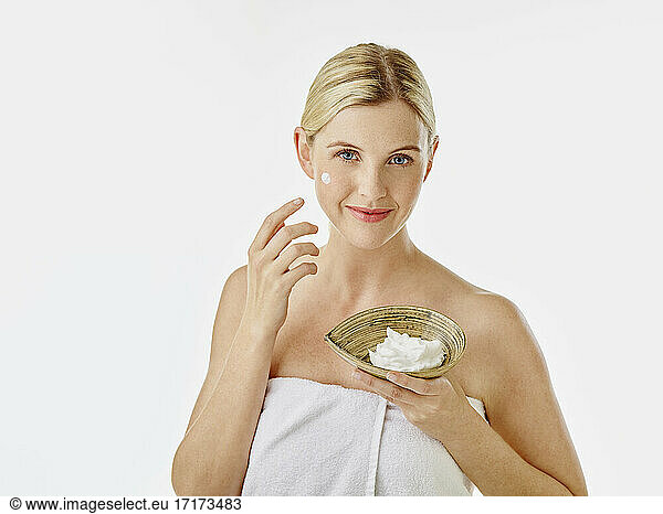 Woman holding face cream bowl while standing against white background