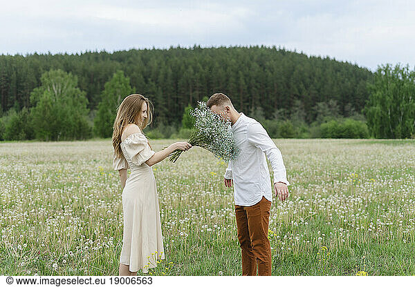Woman holding flower bouquet in front of boyfriend on field