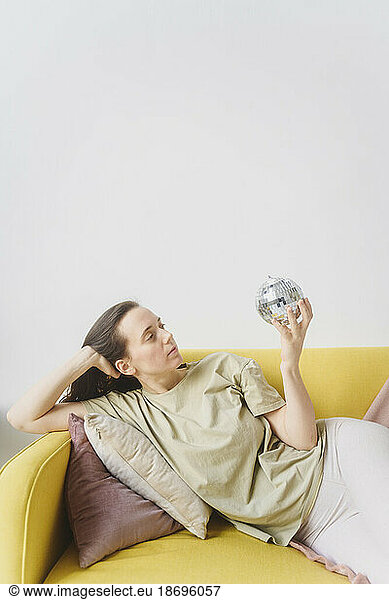 Woman holding glass ball lying on yellow sofa