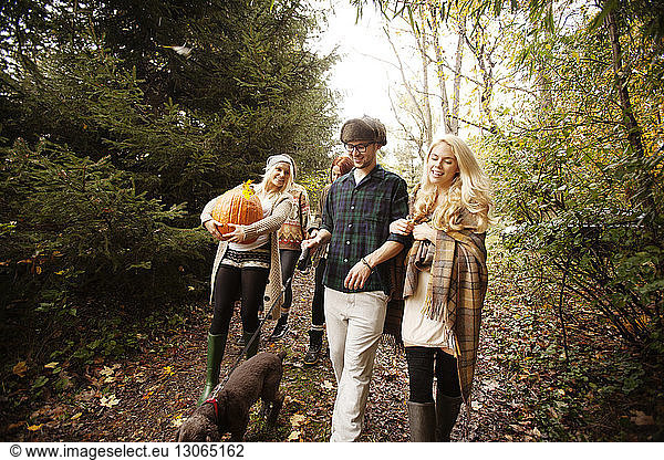 Woman holding Halloween pumpkin while walking with friends in forest