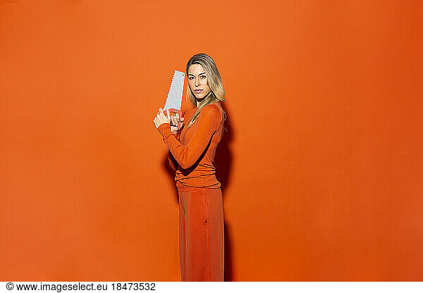 Woman holding hand saw against orange background