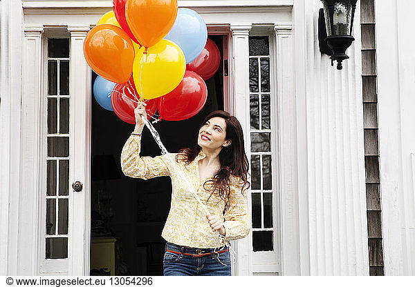 Woman holding helium balloons while standing outside house
