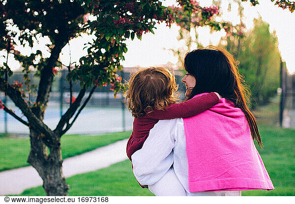 Woman holding her daughter under the tree and smiling