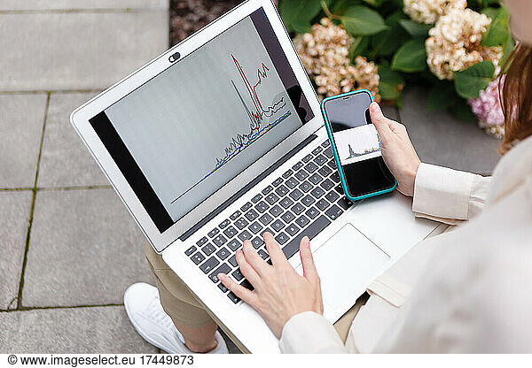 woman holding laptop and smartphone watching bitcoin growth chart