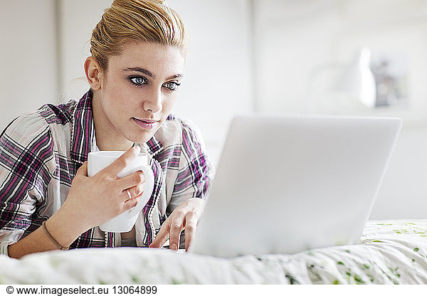 Woman holding mug using laptop computer at home
