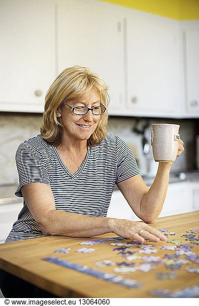 Woman holding mug while playing jigsaw puzzle at home