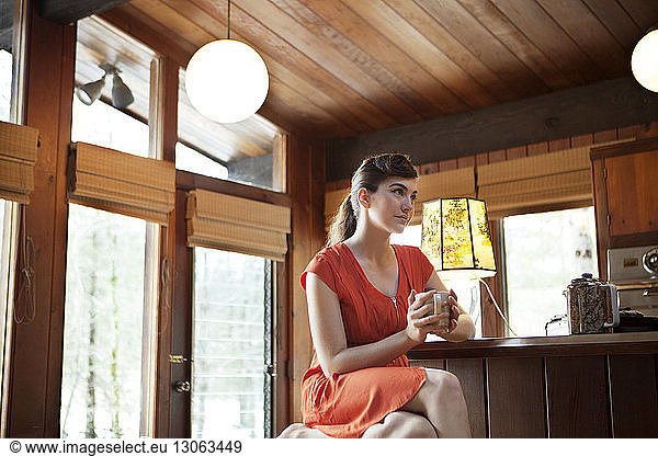 Woman holding mug while sitting by table in cafe
