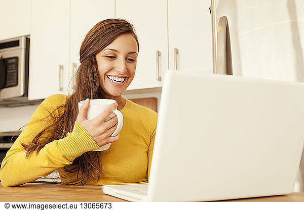 Woman holding mug while using laptop computer at home
