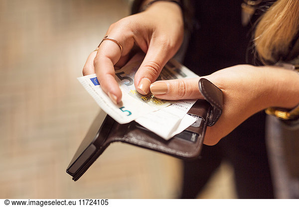 Woman holding open wallet with banknotes  receipts and cell phone