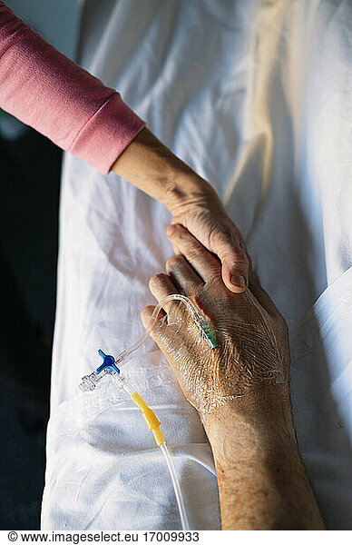 Woman holding patient hand on bed in hospital
