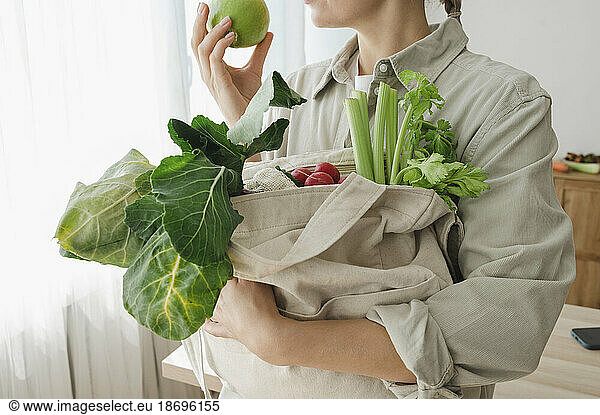 Woman holding reusable bag full of organic vegetables and fruits