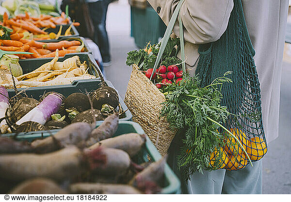 Woman holding shopping bags standing by vegetables in crate