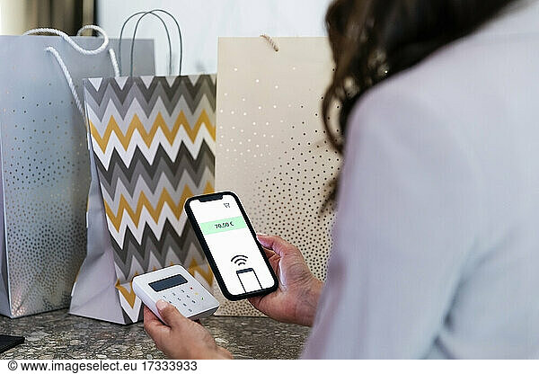 Woman holding smart phone while doing contactless payment in boutique