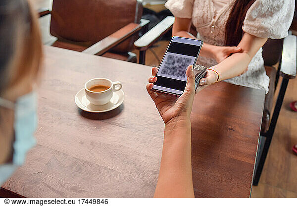 woman holding smartphone close to electronic payment machine