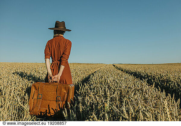 Woman holding suitcase standing amidst wheat field
