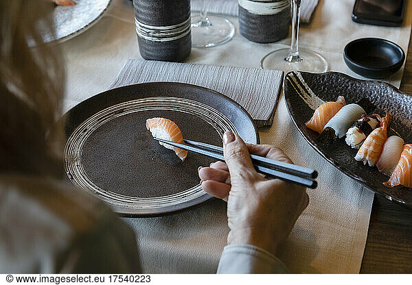 Woman holding sushi with chopsticks at restaurant