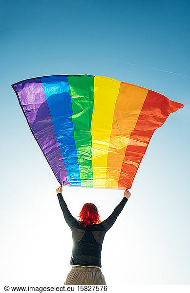 Woman holding the Gay Rainbow Flag on blue sky background. Happiness  freedom and love concept for same sex couples.
