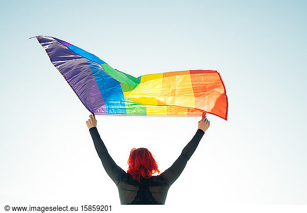 Woman holding the Gay Rainbow Flag on blue sky background. Happiness  freedom and love concept for same sex couples.