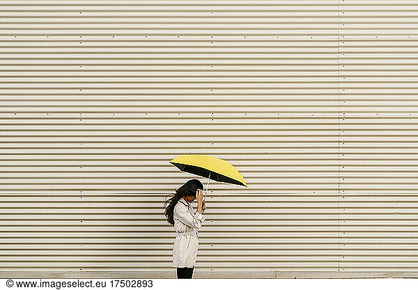 Woman holding umbrella by white corrugated wall